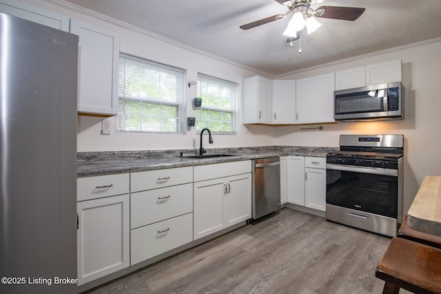 kitchen with stainless steel appliances, a sink, ornamental molding, light wood-type flooring, and white cabinetry