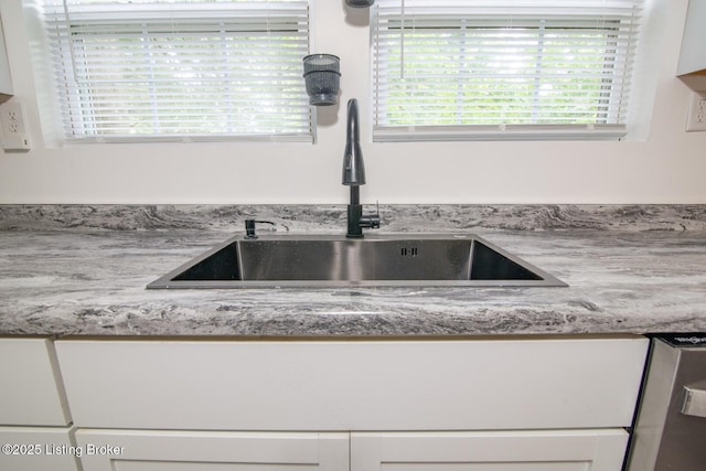 kitchen view of a sink, light stone counters, and white cabinets