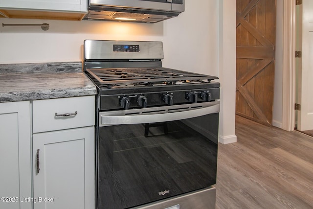 kitchen with stainless steel range with gas cooktop, wood finished floors, white cabinets, and light stone countertops