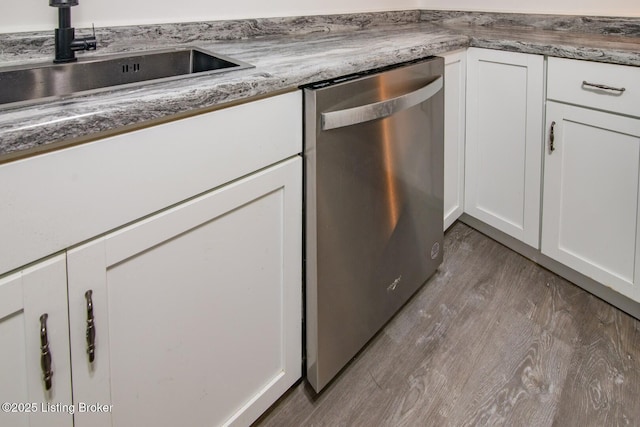 kitchen view of stainless steel dishwasher, white cabinetry, wood finished floors, and a sink