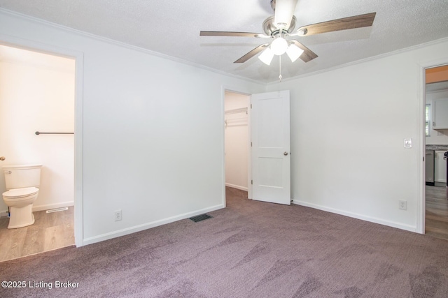 unfurnished bedroom featuring crown molding, carpet floors, ensuite bath, a spacious closet, and baseboards
