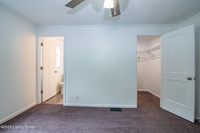 unfurnished bedroom featuring carpet, crown molding, a spacious closet, a closet, and baseboards