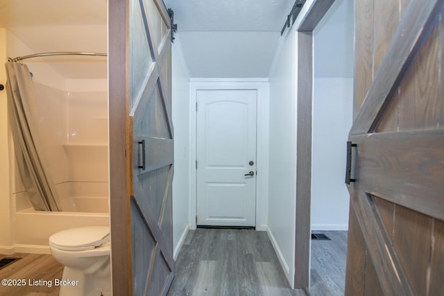 bathroom featuring wood finished floors, baseboards, shower / tub combo, and toilet