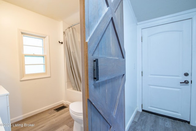 bathroom featuring wood finished floors, baseboards, toilet, vanity, and shower / bathtub combination with curtain