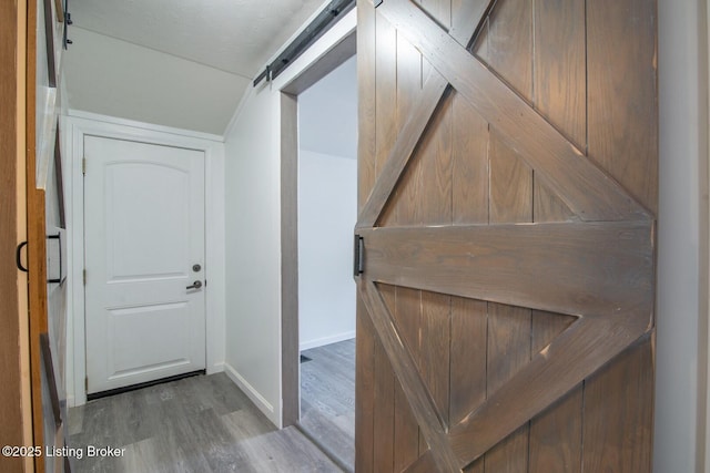 corridor with wood finished floors, baseboards, a barn door, and vaulted ceiling