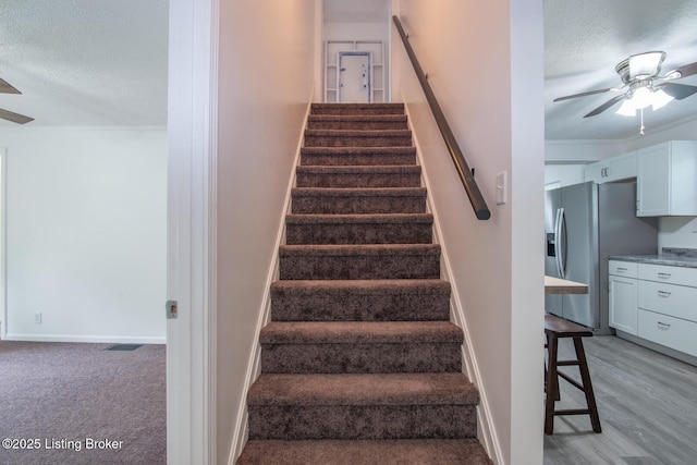 stairway featuring a ceiling fan, a textured ceiling, crown molding, baseboards, and wood finished floors