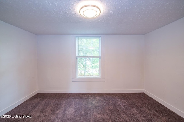 spare room featuring a textured ceiling, baseboards, and dark carpet