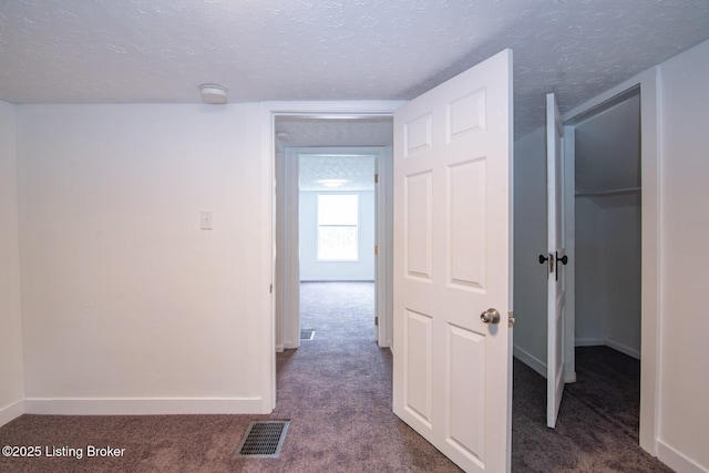 hallway with dark colored carpet, a textured ceiling, and baseboards