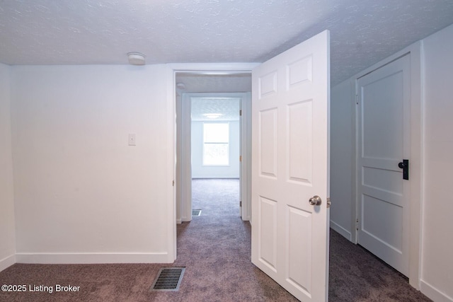 hall with dark carpet, a textured ceiling, and baseboards