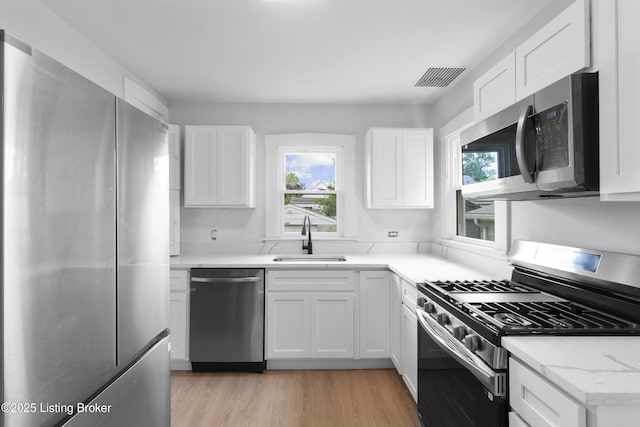 1011 Wetterau Ave, Louisville, KY 40217 - kitchen featuring stainless steel appliances, a sink, white cabinetry, light wood-type flooring, and light stone countertops