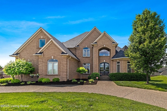 traditional home with french doors, brick siding, a front yard, and roof with shingles