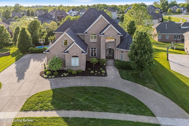 traditional home featuring curved driveway, brick siding, a residential view, a front yard, and roof with shingles