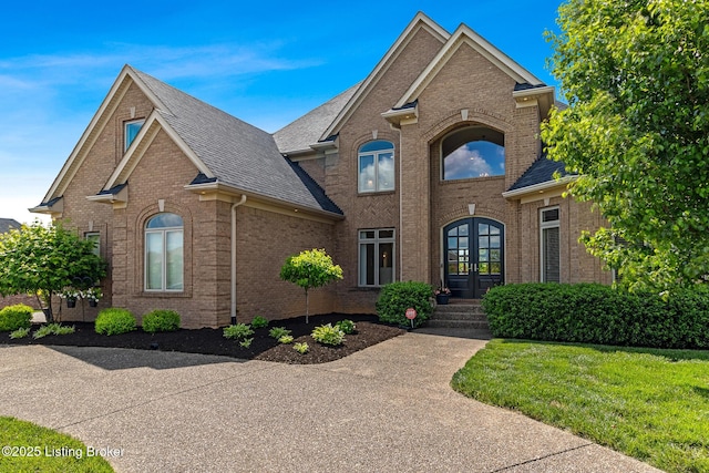 traditional-style home with french doors, brick siding, and roof with shingles