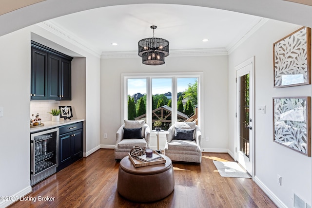 living area featuring beverage cooler, a dry bar, dark wood-style flooring, a chandelier, and crown molding