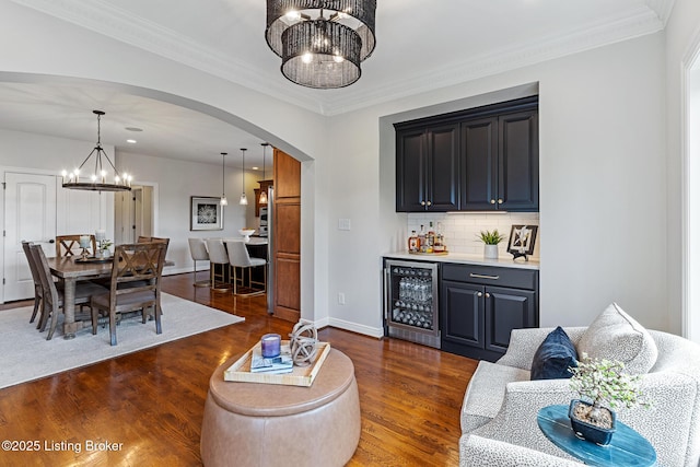 living area featuring beverage cooler, arched walkways, bar with sink, dark wood finished floors, and a chandelier