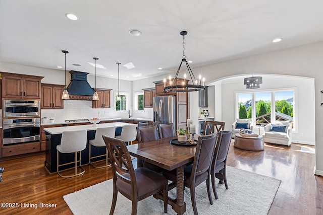 dining space with arched walkways, a chandelier, healthy amount of natural light, recessed lighting, and dark wood-type flooring