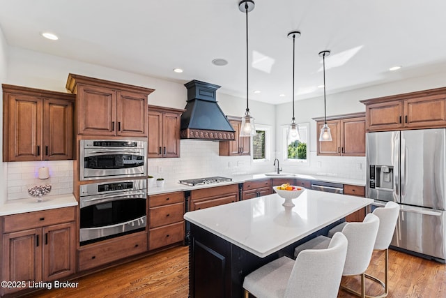 kitchen featuring appliances with stainless steel finishes, custom exhaust hood, decorative backsplash, hanging light fixtures, and a breakfast bar