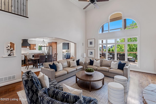 living area with arched walkways, a high ceiling, wood finished floors, ceiling fan, and a chandelier