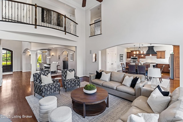 living room with arched walkways, ornamental molding, dark wood-style floors, a chandelier, and baseboards