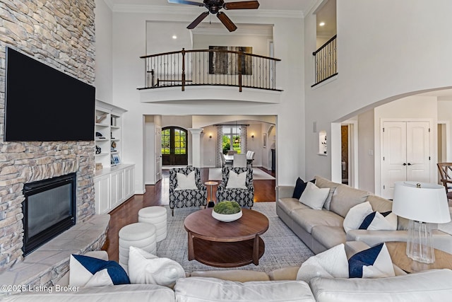 living room with arched walkways, wood finished floors, ceiling fan, a fireplace, and crown molding
