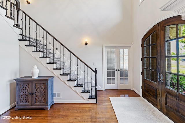 foyer entrance featuring french doors, wood finished floors, stairway, a high ceiling, and baseboards