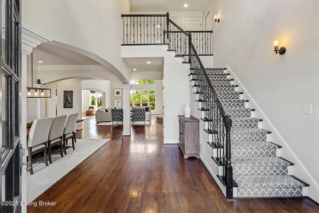 entryway featuring arched walkways, stairs, wood finished floors, a high ceiling, and baseboards