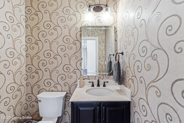 half bathroom featuring wallpapered walls, vanity, and toilet