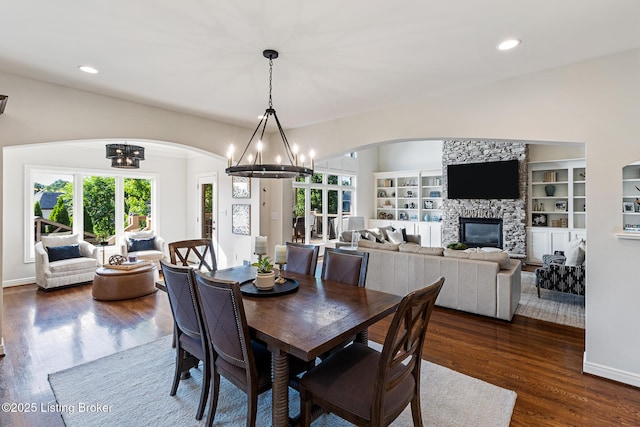 dining space with arched walkways, a chandelier, dark wood-style flooring, recessed lighting, and a fireplace