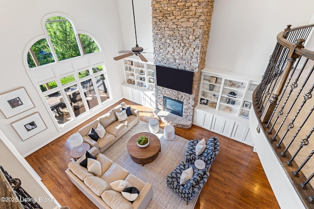 living room with a high ceiling, wood finished floors, a ceiling fan, built in shelves, and stairway