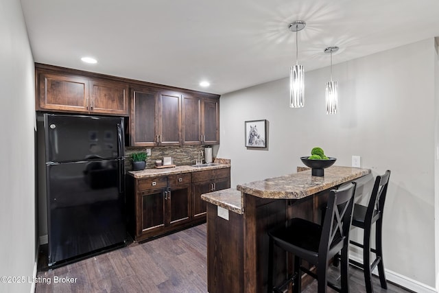 kitchen featuring freestanding refrigerator, dark brown cabinetry, dark wood-type flooring, tasteful backsplash, and a kitchen bar