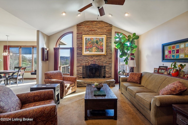 living room with ceiling fan, a stone fireplace, lofted ceiling, light colored carpet, and a chandelier
