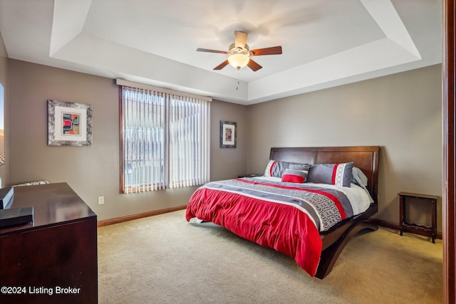 carpeted bedroom featuring a tray ceiling, baseboards, and a ceiling fan