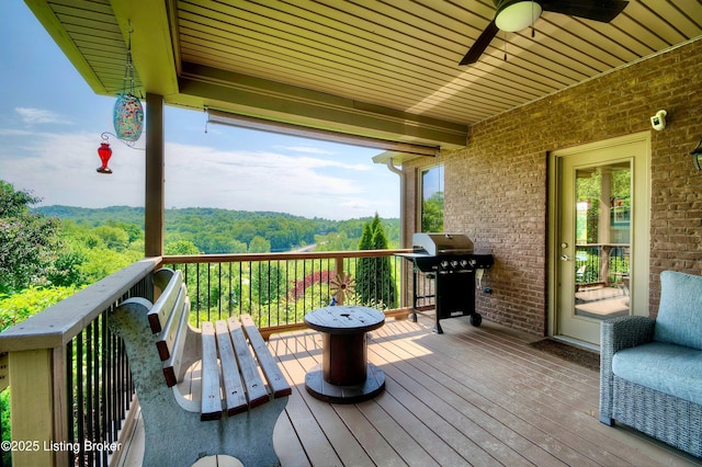 deck with area for grilling, a ceiling fan, and a view of trees