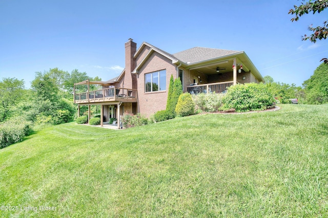 rear view of house featuring a chimney, ceiling fan, a yard, a wooden deck, and brick siding