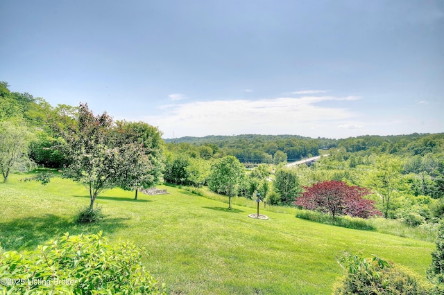 view of green lawn featuring a forest view
