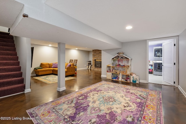 playroom with stacked washing machine and dryer, baseboards, a brick fireplace, and recessed lighting