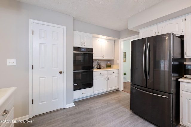 kitchen featuring black appliances, white cabinetry, light countertops, light wood-type flooring, and baseboards