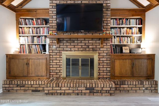 unfurnished living room featuring built in features, vaulted ceiling, wood finished floors, and a fireplace