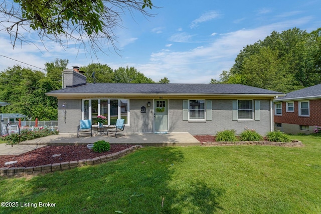 view of front of home with a chimney, brick siding, a front yard, and a patio