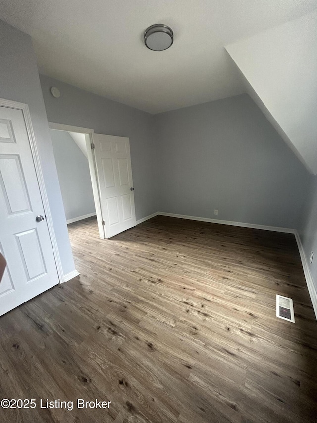 bonus room with dark wood-style flooring, lofted ceiling, and baseboards