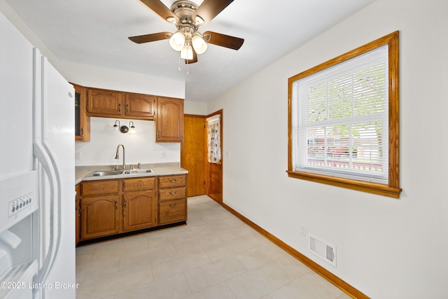 kitchen featuring white refrigerator with ice dispenser, a sink, light countertops, and brown cabinets
