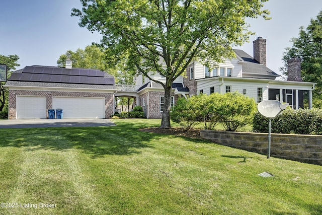 view of front of home featuring a chimney, an attached garage, roof mounted solar panels, and a front lawn
