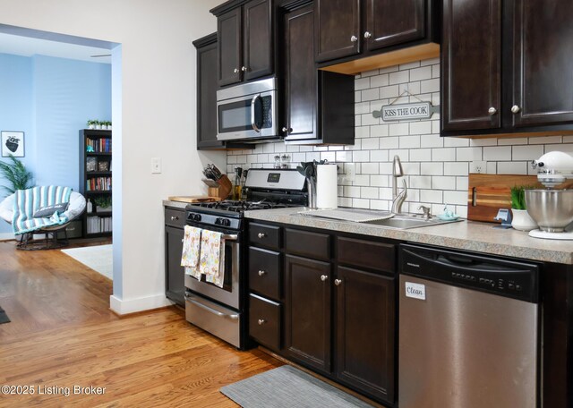 kitchen featuring stainless steel appliances, baseboards, a sink, and light wood finished floors