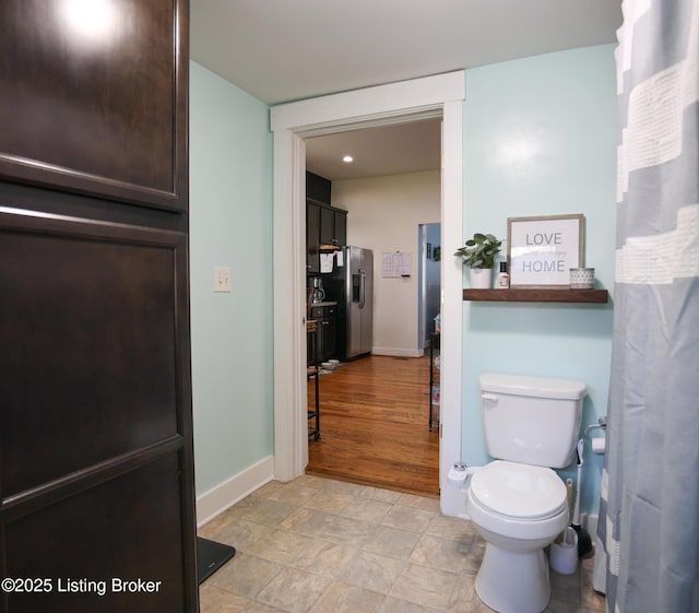 bathroom featuring toilet, stone finish flooring, and baseboards