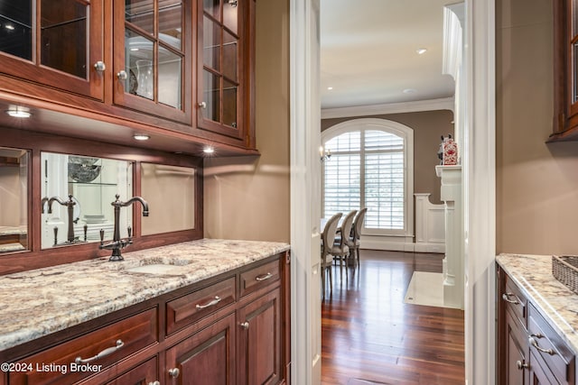 indoor wet bar featuring crown molding, dark wood-style floors, a wainscoted wall, arched walkways, and a decorative wall