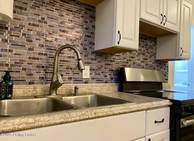 kitchen with range with electric cooktop, a sink, tasteful backsplash, and white cabinetry
