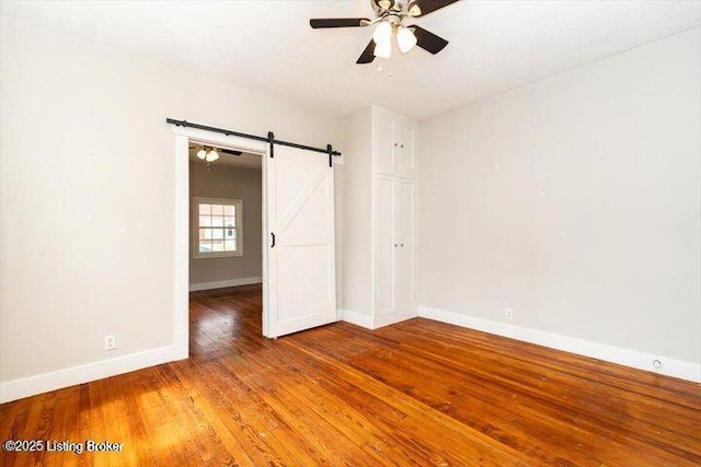 1205 Fischer Ave, Louisville, KY 40204 - unfurnished bedroom with baseboards, a barn door, wood finished floors, and ceiling fan