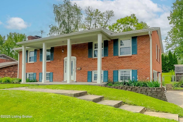 raised ranch featuring a front lawn, covered porch, brick siding, and a chimney