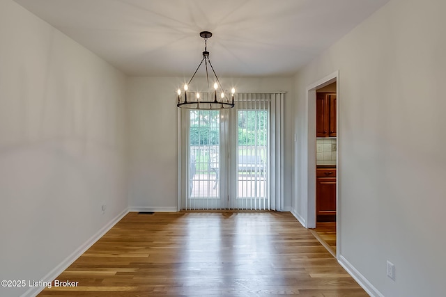 unfurnished dining area with a chandelier, wood finished floors, and baseboards