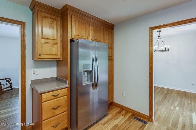 kitchen with stainless steel fridge, light wood-style flooring, a chandelier, brown cabinetry, and baseboards